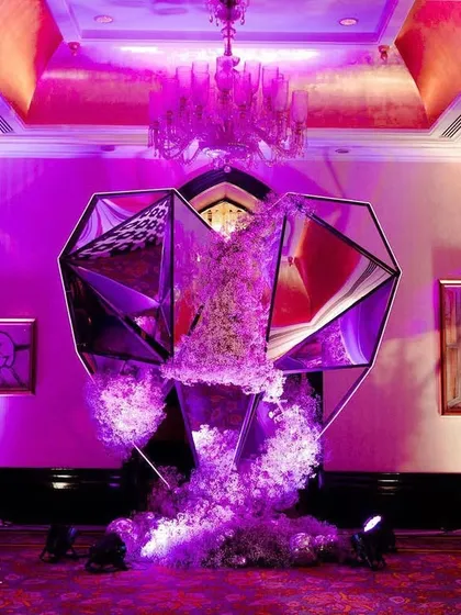 A dramatic, geometric art installation for the Sangeet entrance, made of mirrored panels and overflowing with flowers. This piece was designed to be a statement of modern art and glamour.