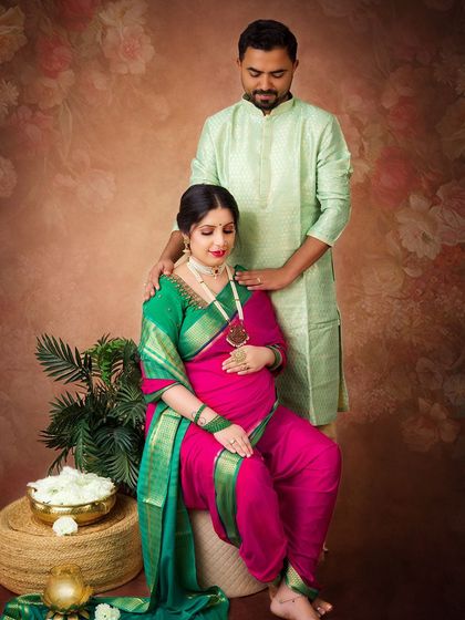 A full-length view of a traditional maternity portrait. The rich pink and green saree and classic props create a culturally rich and beautiful image.