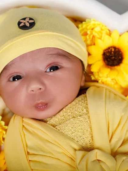 An adorable awake newborn with a "pouty face" expression, nestled amongst sunflowers.
