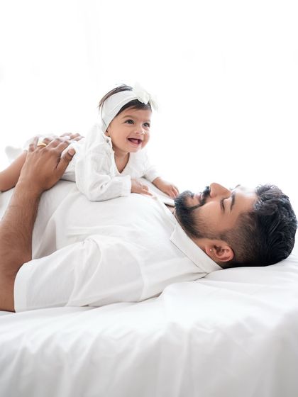 A father and baby enjoying a happy moment together on a bright white bed.