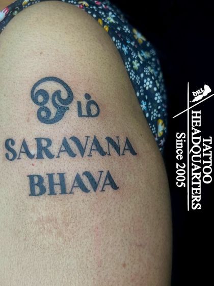 A spiritual tattoo with "Om" in Tamil script and the mantra "Saravana Bhava" in English, honoring Lord Murugan.