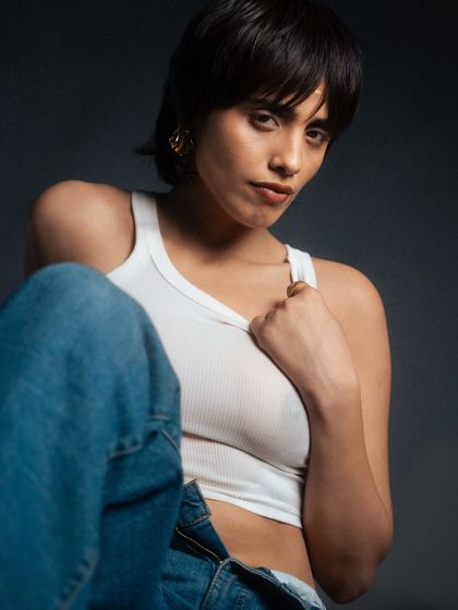 A close-up portrait with soft, directional lighting. This shot focuses on the model's expression and the simple styling of the white tank and jeans, creating an intimate and authentic feel.