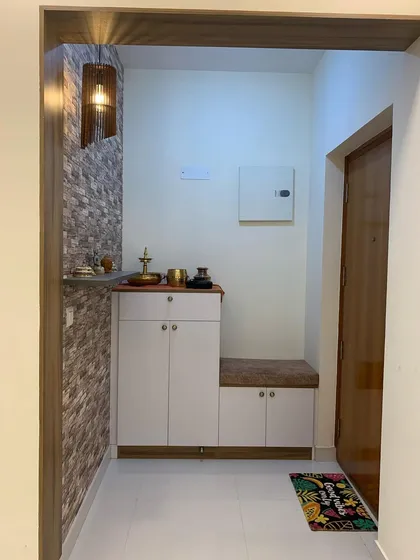 The foyer entrance of this apartment features a practical shoe rack with seating, set against a stone-cladding wallpaper. This small space is designed to be both welcoming and highly functional.