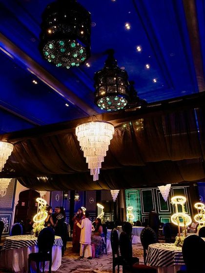 A grand view of the indoor Sangeet, where the deep blue of the venue's walls is complemented by black drapes and dozens of sparkling chandeliers.