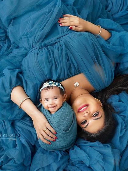 A happy baby girl, just 30 days old, smiles up at the camera while being cradled by her mother. This overhead shot on a beautiful blue fabric captures a truly precious and rare moment.