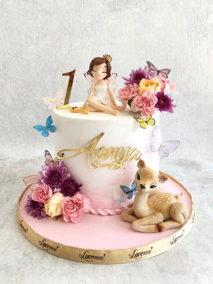 A whimsical woodland fairy cake for Aanya's first birthday. This cake features a sweet fairy figurine, a baby deer, and is adorned with fresh flowers and edible butterflies.