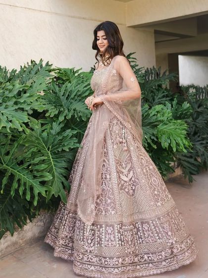 A model posing in a beautiful dusty pink lehenga with all-over silver embroidery. This is a classic and elegant choice for an engagement or reception.
