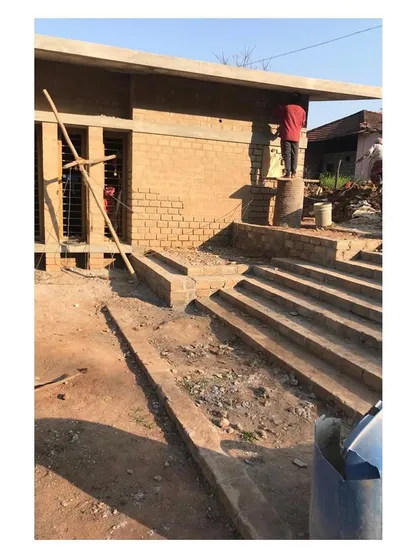 A worker applies finishing touches to the mud brick walls. The stepped entrance, a common feature in traditional Indian architecture, is also visible, providing informal seating.