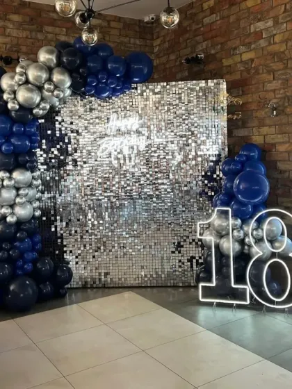 An 18th birthday party with a silver sequin wall, a neon "18", and a balloon arch in dark blue and silver.