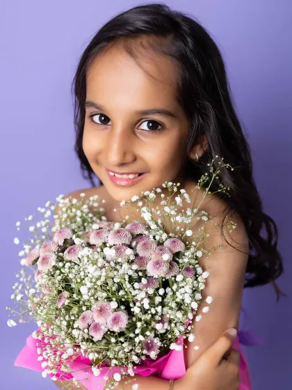 A close-up of her beautiful smile, holding the flowers close. The soft colors and creative concept make this a stunning and unique kid portrait.