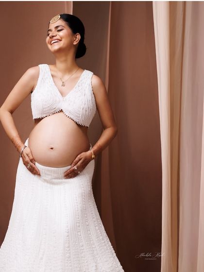 A joyful and radiant smile captured in a modern white two-piece outfit, celebrating the bare bump with elegance.