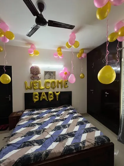 Even a simple setup can feel special. Here, I decorated the bedroom with 'Welcome Baby' foil balloons and scattered pink and yellow balloon clusters on the ceiling for a happy, festive feel.