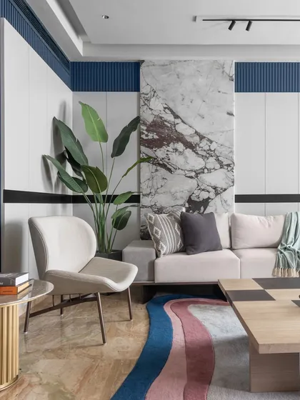 A detail shot of the living room corner, where a statement marble panel contrasts with the blue fluted wall. A comfortable accent chair and side table create a perfect reading nook.