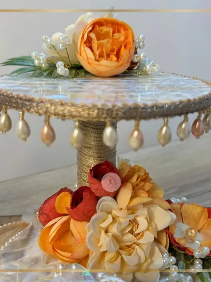 A detailed view of the two-tiered stand from our mother-of-pearl ring platter set. The dangling pearl details and the vibrant orange flower on top create a stunning focal point for the ceremony.