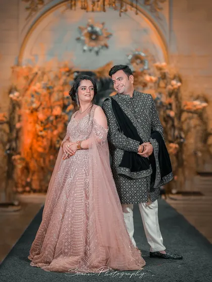 A full-length portrait of a couple at their engagement, posing elegantly in a grand, beautifully lit hall.