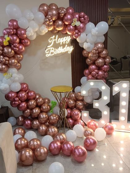 A beautiful rose gold and white theme for a 31st birthday. The setup features a balloon ring, a neon sign, and large light-up marquee numbers, perfect for photos.