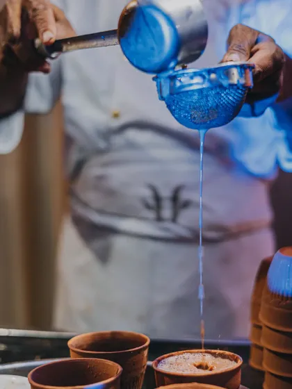 The simple art of making perfect masala chai. A chef strains freshly brewed tea into traditional kulhads, ready to serve guests a warm and comforting beverage, perfect for any weather.