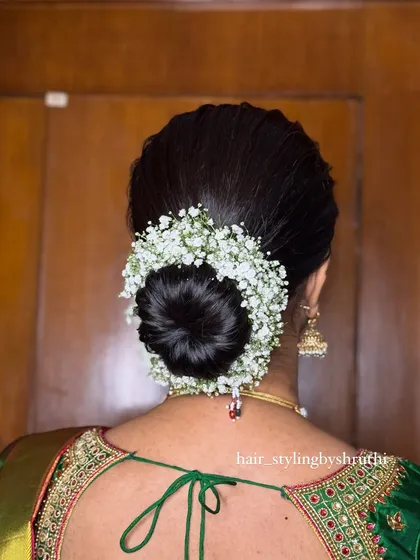 A perfectly neat and classic bridal bun, encircled with a halo of fresh baby's breath gajra. This timeless updo is a popular choice for its simple elegance and is ideal for South Indian wedding ceremonies.
