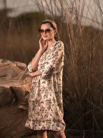 A relaxed, three-quarter shot of a model in a printed dress, set against tall, wild grass. The soft, natural lighting is ideal for showcasing resort wear and summer collections.