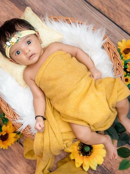 A continuation of the sunflower theme, this shot shows the baby swaddled and lying peacefully in a basket. The wooden floor and bright yellow flowers create a warm, rustic, and cheerful atmosphere.