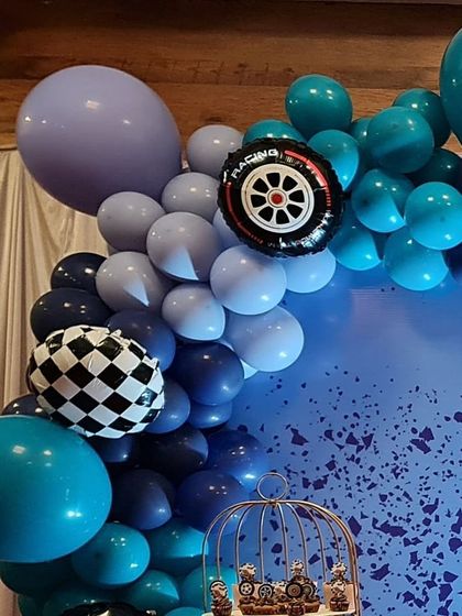 A detailed shot of a race car-themed balloon garland. The arrangement includes shades of blue and is accented with a checkered balloon and a foil racing wheel balloon.