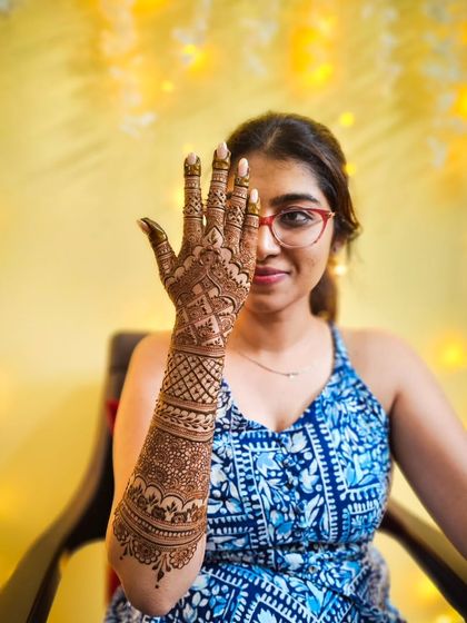 A stylish one-eyed pose highlighting the detailed henna work on the back of the hand and arm.