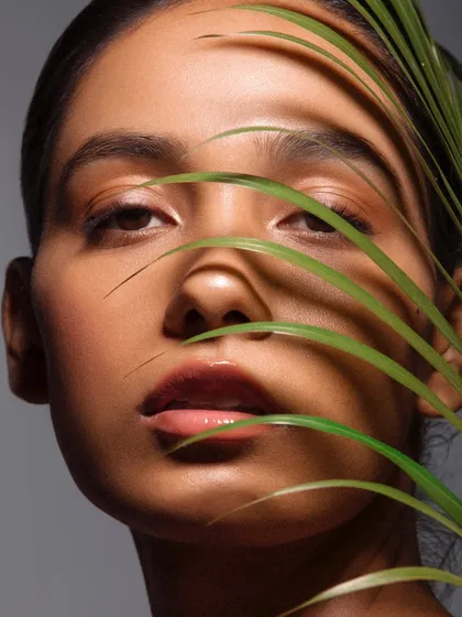 A simple, clean beauty look with glowing skin, enhanced by the natural pattern of a palm leaf. This shows the power of minimalist artistry.