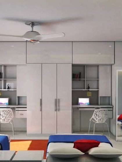 This design for a shared room features two beds with a central wardrobe unit that also houses two individual study desks. The clean, glossy white finish makes the room feel bright and spacious.