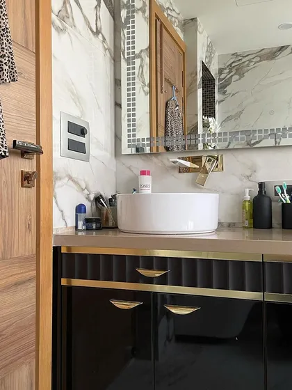 A side view of the Calacatta marble bathroom, showing the contrast between the black vanity, the white vessel sink, and the warm wood of the door.