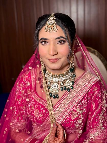 Vidhi, a picture of bridal grace. Her makeup is kept soft and radiant to complement her pink lehenga and emerald jewelry.