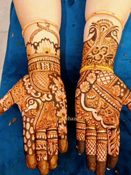 A pair of hands with matching traditional mehandi, featuring peacocks, lotuses, and intricate filler patterns.