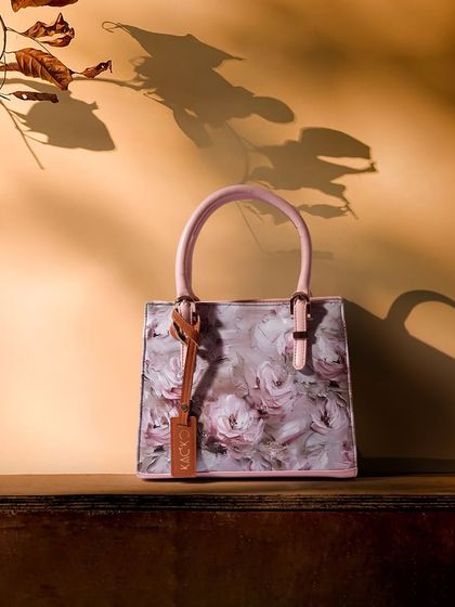 A floral handbag captured in warm, golden-hour light. The shadows of leaves add a natural, artistic element to the composition.