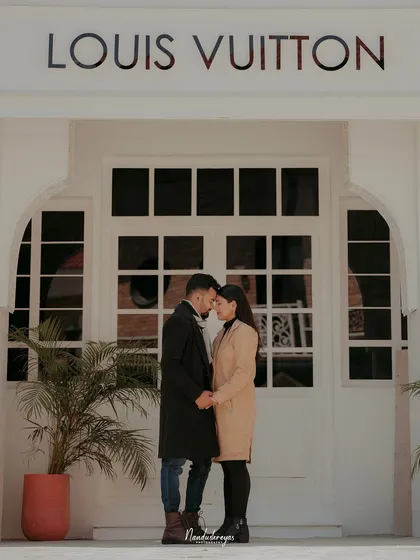 A chic, fashion-inspired shot of a couple holding hands in front of a storefront with European-style architecture, perfect for an urban glam look.