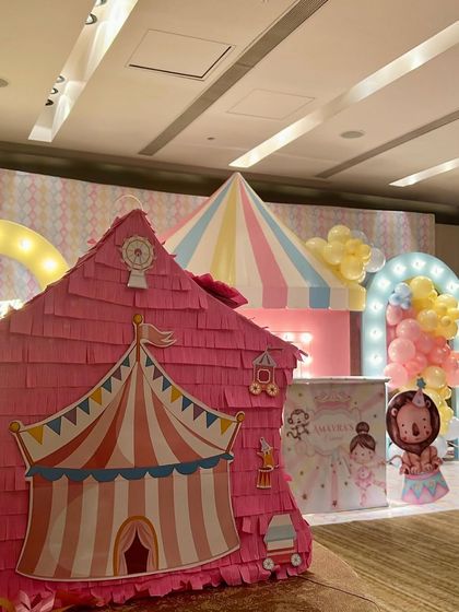 Kicking off the holiday season with a festive carnival-themed birthday. This indoor setup features a pink circus tent prop, a striped concession stand, and marquee lights for a whimsical party atmosphere.