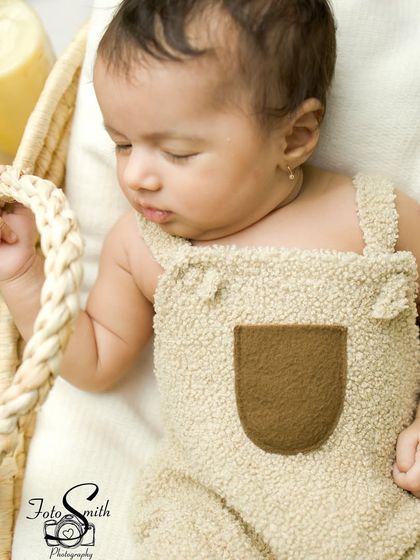 A sleeping baby in a textured beige outfit, resting in a basket. The overhead lighting beautifully highlights the baby's peaceful features.