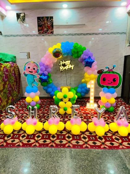 Another fun Cocomelon first birthday, this time with the name "SHREYA" spelled out in balloons. The setup includes a circular balloon arch, character stands, and a light-up '1'.
