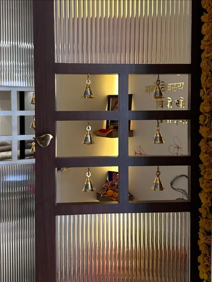 A side view of the pooja room door, showing the detail of the bird-shaped handle and the warm glow from within.