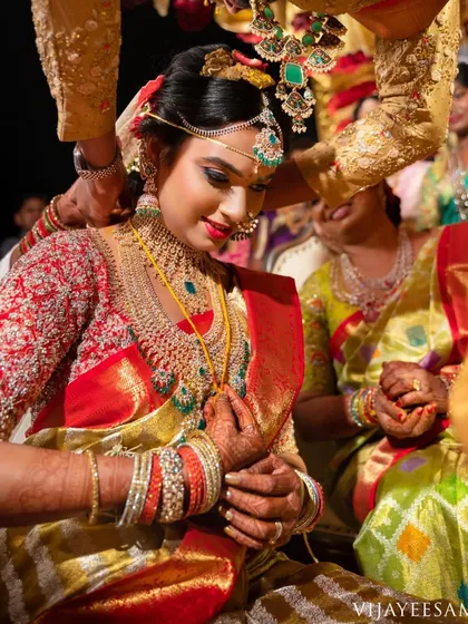 A candid moment from a wedding ceremony. The bride's red embroidered blouse is a key element of her traditional and opulent look.