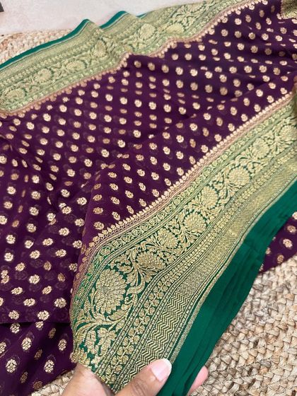 A deep wine-purple Kadi georgette saree with a contrasting green border. The gold butis and floral vine on the border add a touch of grace.