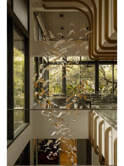 A residential interior by N G Associates, shortlisted at WAF. This image showcases a stunning, multi-story cascading light fixture made of glass birds, which fills the home's central void with art and light.