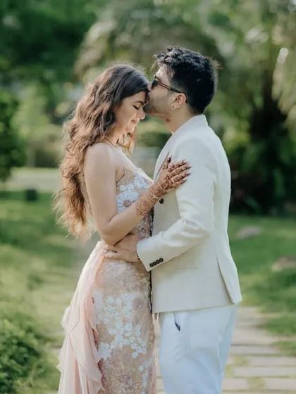 A sweet and affectionate portrait. The groom's gentle kiss on the bride's forehead captures a moment of pure love and happiness amidst the greenery of their party venue.