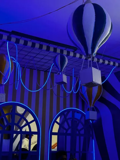 The evening ambiance of our Uttarayan party, featuring miniature hot air balloon props and blue neon light accents. This created a dreamy and magical atmosphere against the striped walls.