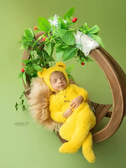 A peaceful newborn portrait of a baby sleeping soundly in a cozy yellow bear outfit. This image showcases my gentle approach to newborn photography, using soft props like a fuzzy blanket and a wooden swing to create a safe and adorable setting.