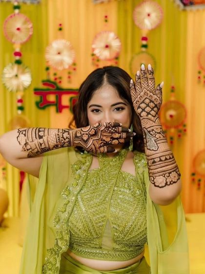 A classic mehendi pose, with the bride playfully hiding her face behind her beautifully decorated hands.