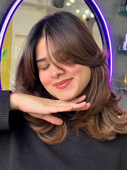 A close-up of a soft brown balayage with face-framing highlights. Notice how the color catches the light and adds dimension, styled with a bouncy, layered blowout.
