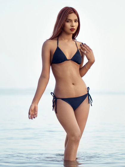 A classic swimwear shot with the model standing in the ocean. The calm water and overcast sky create a soft, even light that is very flattering.