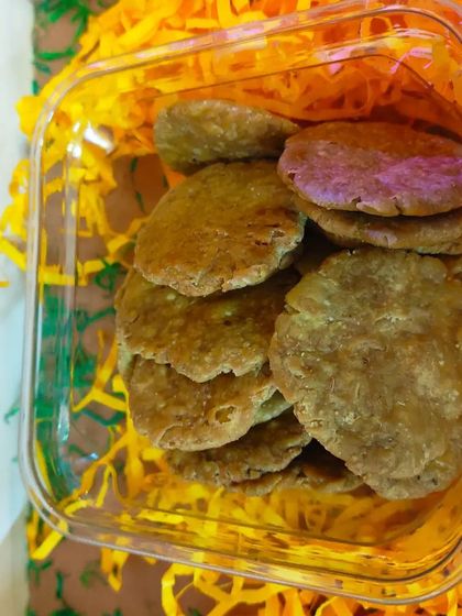 A close-up of the savory Spinach Mathri, packed in a clear box and nestled in yellow paper shred.