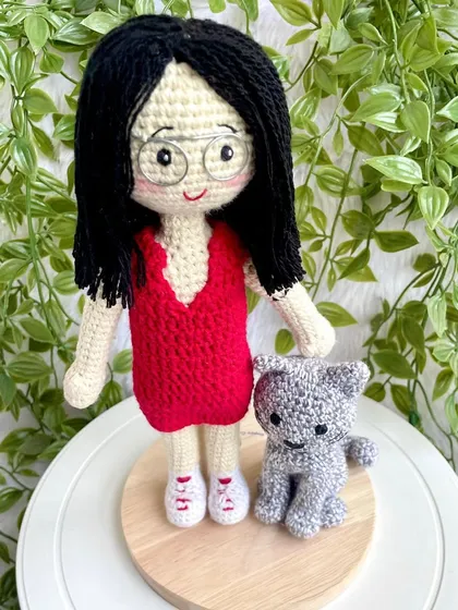 A thoughtful farewell gift for a niece heading off to higher studies. This replica doll in a red dress stands with her pet cat on a display base, a reminder of home she can take with her.