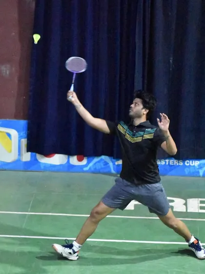 A player reaching for a clear, demonstrating the full extension and footwork needed to control the rally from the backcourt.