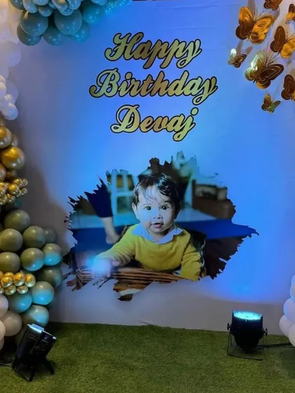 A personalized birthday backdrop featuring a photo of the birthday boy. The backdrop is framed with a sage green and gold balloon arch and accented with butterfly details.